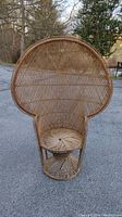 Front view of large vintage wicker peacock chair outdoors on pavement showing full seat, backrest, and base structure