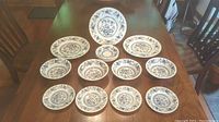 Full set of 15 dinnerware pieces including 3 dinner plates, 4 cereal bowls, 4 bread/butter plates, and 4 saucers laid out on a wooden table.
