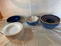 Full view of bowls and plates showing white soup bowls stacked on left, blue nested bowls on right, flower-shaped bowl center, and additional bowls in front