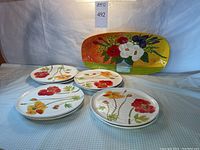 Overview photo showing Vietri Italy oval serving platter with colorful floral design behind seven round Crate & Barrel floral dinner plates arranged in front on table.