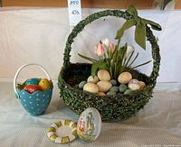 Front view of green faux foliage basket with artificial tulips and speckled eggs, turquoise polka dot basket with glass eggs, porcelain bunny egg, and small round plate.