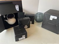 Display of two boxed porcelain teapot sets, sugar and creamer sets, and etched glass vase with original packaging.