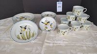 8 shallow bowls stacked, 8 mugs grouped together, 8 dessert plates with varied bird designs shown spread out