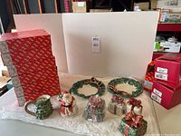 Displays all holiday porcelain items including 8 canap plates, Santa figurine, several lidded boxes, and original Fitz & Floyd boxes in background.