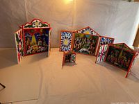 Three Peruvian folk art retablos displayed with open hinged doors showing colorful interior narrative scenes and painted floral exterior designs against a neutral backdrop.