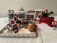 Photo showing multiple Christmas ornaments including Hallmark Keepsake cars in boxes, Annalee Santa in sleigh and clown figures, and other assorted decorations.
