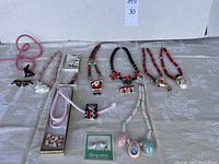 Overview of multiple handcrafted glazed ceramic costume jewelry pieces arranged on fabric backdrop including Christmas and Easter themed necklaces, earrings, and brooch.