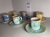 Five small hand painted Italian ceramic teacups on matching saucers arranged in a row, varied bright colors and designs