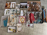 Wide view of all jewelry included in the lot showing various necklaces, bracelets, brooches, and earrings arranged in boxes and trays on the floor.