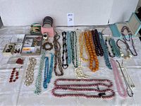 Full view of costume jewelry including necklaces, bracelets, earrings, brooches, and watch laid out on a white cloth surface.