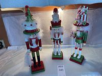 Three Kurt S. Adler nutcracker figurines with Christmas themes and glitter, arranged standing side by side