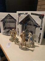 Photo showing two dark wood nativity stable frames in packaging and several Lenox porcelain nativity figures on table including Mary, Joseph, two angels and donkey.