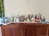Full layout of holiday village houses and decorations on wooden cabinet with artificial snow packs visible.