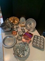 Full view of assorted metal baking tins and cookie cutters arranged on table including Bundt pans, angel food cake pans, muffin tins, cookie cutters, and various mini cake molds.