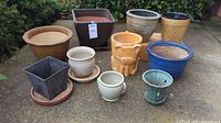 Full lot of 9 assorted ceramic and terracotta plant pots arranged on the ground outdoors.