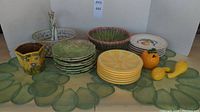 Full lot view showing various ceramic plates, bowls, and decorative pieces on a green scallop-patterned cloth.
