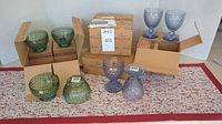 Green crystal bowls and blue stemmed goblets displayed in open boxes, new in packaging.