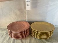 Two stacks of dinner plates, one pink stack and one yellow stack, both with raised vine and floral pattern, ribbed edges visible, 16 plates per stack.