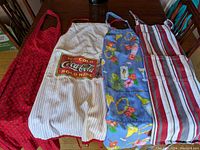 Four aprons laid out side by side on a wooden table showing different designs and colors.