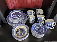 Photo showing stacked blue and white china including plates, bowls, cups, and saucers arranged on black surface with red background.