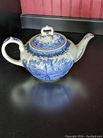 Single blue and white ceramic teapot with attached lid, detailed scenic blue floral and landscape design, shown on black surface.