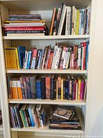 Photo of bookshelf showing travel books and atlases on top shelf, various novels on middle shelves and specialty books