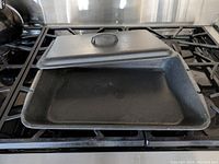 Opened cast iron roaster on gas stove showing inside surface and lid placed partially on roaster.