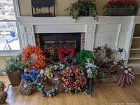 Wide view of wreath collection in front of fireplace showing 19 pieces with multiple colors and seasonal themes including fall, winter, and patriotic.