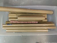 Multiple rolls of brown kraft wrapping paper, some with patterns, placed in a plastic container on the floor