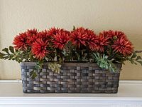 Front view of silk flower arrangement with red-orange blooms and green leaves in a rectangular woven basket