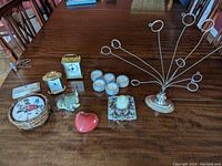 Photo of decorative lot items including small clocks, coaster set with holder, candle holders, card holder, and red heart figurine arranged on a wooden table.