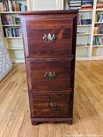 Front view of a dark solid wood 3-drawer file cabinet with ornate handles, closed drawers.