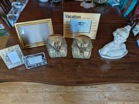 Photo of all lot items on wooden table including three decorative frames, two sphinx bookends, and bust sculpture.