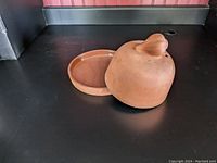Full side view of terracotta garlic roaster with lid resting beside the base dish on a black surface.