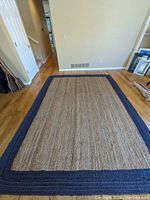 Full view of large rectangular area rug with dark blue border on hardwood floor.