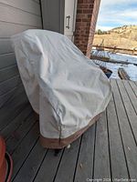 Outdoor chair cover on patio chair showing beige upper fabric and brown bottom section, cover fits large chair tightly.