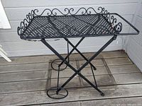 Side angled view showing foldable X-shaped legs, wheels, and decorative scrollwork on tray edges.