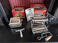 Full set displayed with boxes and instruction leaflet, showing pasta roller and ravioli maker tools with chrome and wood finish.
