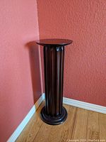 Full view of the black painted wooden plant stand placed against a textured red wall and on wooden floor.