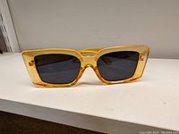 Photo showing one pair of rectangular retro sunglasses with yellow amber translucent plastic frame and dark lenses.