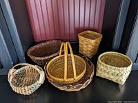 Five assorted serving baskets shown together, different shapes and sizes visible, arranged on dark surface against reddish background panel.