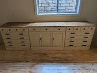 Front view of three matching distressed white dressers with top drawers and larger bottom drawers and central cabinet with louvered doors under window