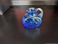 Photo showing the front and side view of the small blue glass pitcher with textured pattern and clear handle.