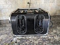 Front view of a Black & Decker 4-slice toaster showing two lever switches and two control dials with settings, on a kitchen counter.