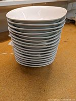 Stack of 16 white bowls shown from the side, highlighting uniform size and shape.