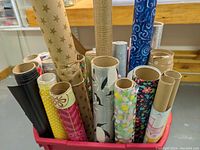 Photo showing an assortment of wrapping paper rolls with diverse designs stored in a red plastic container