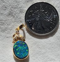 Front of opal pendant next to Canadian quarter to show size; blue-green opal with gold bezel and white stone leaves.