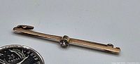 Full view of the antique 9ct gold pin with clear stone next to a quarter for size reference.