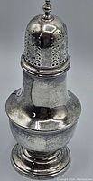 Front view of the silver shaker with perforated domed lid and finial knob.