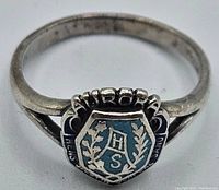 Ring front detail showing shield-shaped top with blue enamel and engraved initials "H S" with laurel branches.